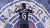a man in a rothwell jersey stands in front of a large rangers logo