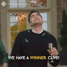 a man holding a glass of wine with the words we have a winner clive below him