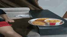 a bowl of chicken nuggets and a hamburger sit on a table next to a person 's leg