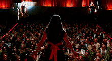 a woman is standing in front of a crowd and pointing at something