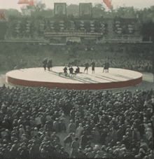 a crowd of people are gathered around a stage with a sign that says ' a ' on it in the background