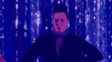 a man is standing on a stage with his hands on his hips in front of a curtain .
