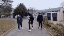 three people are walking down a sidewalk wearing masks and holding sticks .