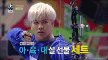 a man in a blue shirt is holding a bow and arrow in front of a sign that says archery