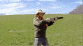 a man in a cowboy hat holds a gun in a grassy field