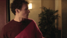 a man in a red sweater is standing in a room with a plant in the background