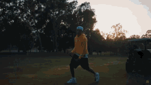 a man in a yellow hoodie and white hat is holding a golf club in a park