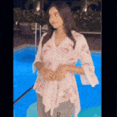 a woman is standing in front of a swimming pool wearing a floral shirt .