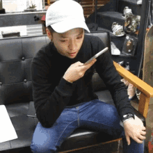 a man wearing a white hat sits on a couch looking at his cell phone
