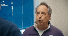 a man in a purple jacket is talking to another man in a blue shirt .