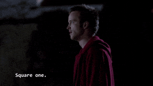 a man in a red hoodie is standing in a dark room with the words square one above him