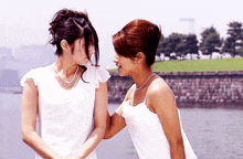 two women standing next to each other with one wearing a necklace