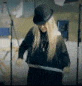 a woman wearing a black hat and a black shirt is standing in front of a microphone .