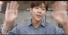 a young man in a plaid shirt is waving his hands in front of a camera .