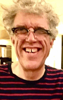 a man wearing glasses and a striped shirt is smiling for the camera