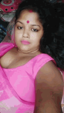 a woman in a pink top with a red dot on her forehead is taking a selfie .