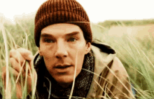 a man wearing a beanie and scarf is standing in the grass .