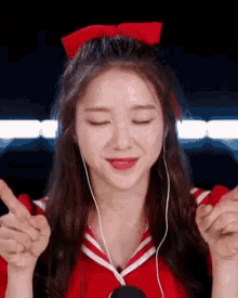 a girl wearing headphones and a red bow in her hair is making a heart with her hands .
