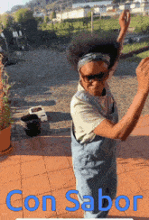 a woman in overalls is dancing on a patio with the words con sabor written below her