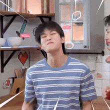 a man in a blue striped shirt is making a funny face in a kitchen .