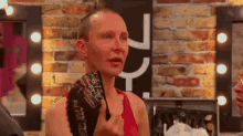 a man with a shaved head is holding a purse in front of a brick wall and mirror .