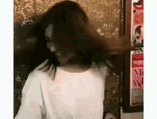 a woman is standing in front of a wall with her hair blowing in the wind while wearing a white shirt .