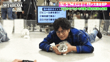 a man laying on the floor holding a cat in front of an abema tv screen
