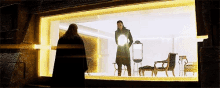 a man in a black coat is standing in front of a window holding a light ..