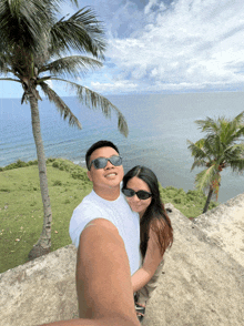 a man and a woman wearing sunglasses pose for a picture in front of the ocean