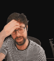 a man with a beard and glasses is holding his head .