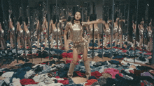 a woman in a gold dress is standing in front of a mirror surrounded by clothes
