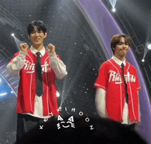 two young men are standing on a stage wearing red baseball jerseys with the word rhythm on them .