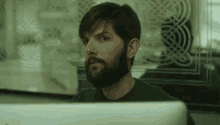a man with a beard is looking at a computer monitor .