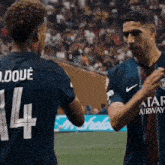two soccer players are shaking hands and one has the number 14 on his jersey