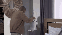 a man in a brown jacket is standing in front of a mirror and a lamp while asking " pretty "