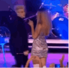 a woman in a silver dress is singing into a microphone while a man stands behind her .