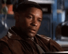 a man in a brown leather jacket is sitting at a table with his hands on his hips .
