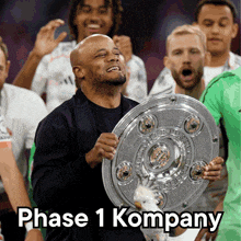a man holding a trophy with the words " phase 1 kompany " on the bottom