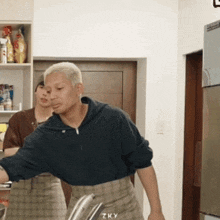 a man standing in a kitchen with zky written on the bottom