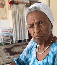 an elderly woman wearing a blue shirt and pearls making a face