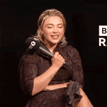 a woman laughs while holding a microphone with the letter b on the bottom