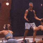 a man in a black tank top and striped shorts stands in front of a woman
