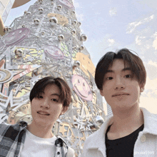 two young men are posing for a picture in front of a large christmas tree