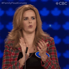 a woman applauds in front of a microphone while wearing a plaid jacket and a black top