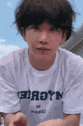 a young man with short hair is wearing a white t-shirt that says ' aoyn ' on it .