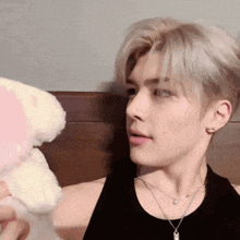 a man wearing a black tank top and a necklace holds a stuffed animal
