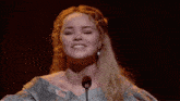 a woman singing into a microphone with a cross necklace