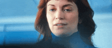 a woman with red hair and blue eyes is wearing a blue turtleneck sweater .