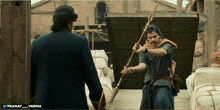 a man holding a spear is standing next to another man with the name pranay on the bottom left