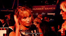 a woman is talking into a microphone in front of a sign that says the hunger games